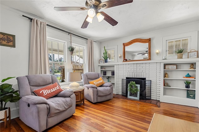 interior space with a textured ceiling, a brick fireplace, ceiling fan, and light hardwood / wood-style flooring