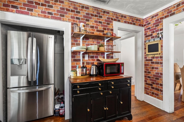 kitchen with crown molding, brick wall, stainless steel fridge, and dark hardwood / wood-style flooring