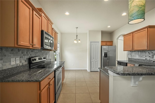 kitchen with hanging light fixtures, light tile patterned floors, sink, stainless steel appliances, and dark stone countertops