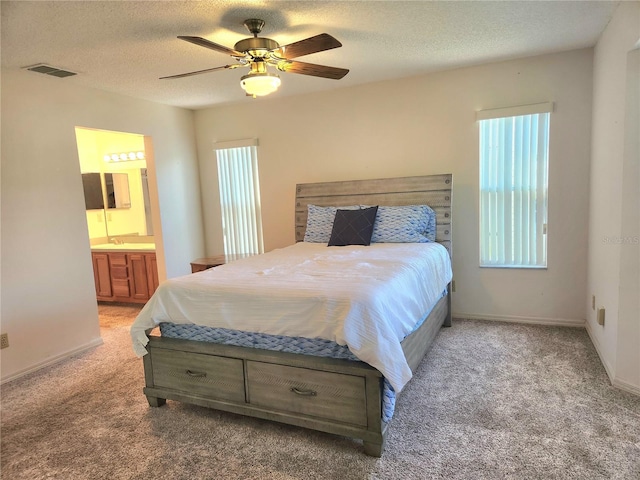 bedroom featuring light carpet, a textured ceiling, ensuite bath, and visible vents