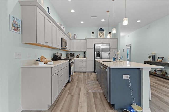 kitchen featuring an island with sink, sink, decorative light fixtures, stainless steel appliances, and light hardwood / wood-style floors