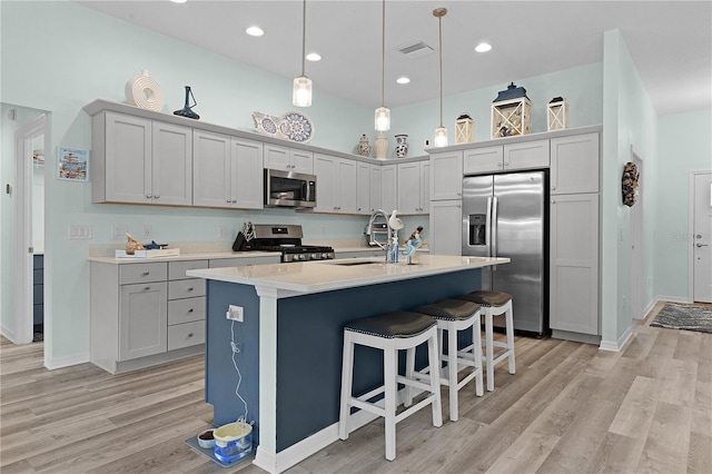 kitchen with pendant lighting, sink, a kitchen island with sink, appliances with stainless steel finishes, and light wood-type flooring