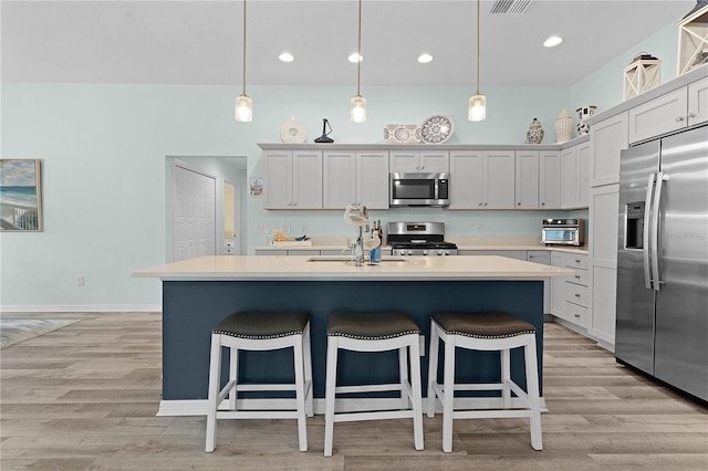 kitchen with an island with sink, appliances with stainless steel finishes, hanging light fixtures, and light hardwood / wood-style flooring