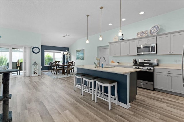 kitchen featuring an island with sink, stainless steel appliances, lofted ceiling, decorative light fixtures, and sink