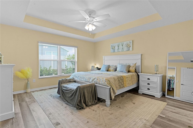 bedroom with light wood-type flooring, a tray ceiling, and ceiling fan