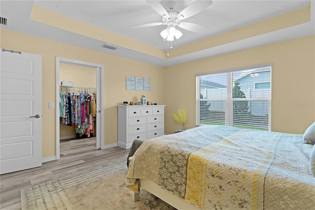 bedroom featuring a closet, light hardwood / wood-style floors, a raised ceiling, a walk in closet, and ceiling fan