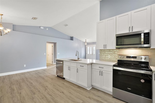 kitchen with white cabinets, sink, stainless steel appliances, an inviting chandelier, and vaulted ceiling