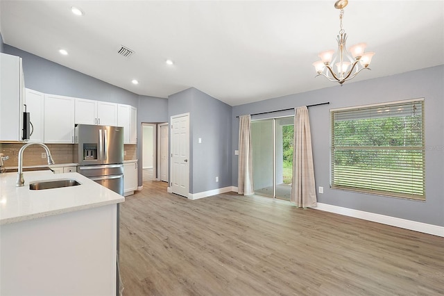 kitchen with vaulted ceiling, light stone counters, hanging light fixtures, white cabinets, and appliances with stainless steel finishes