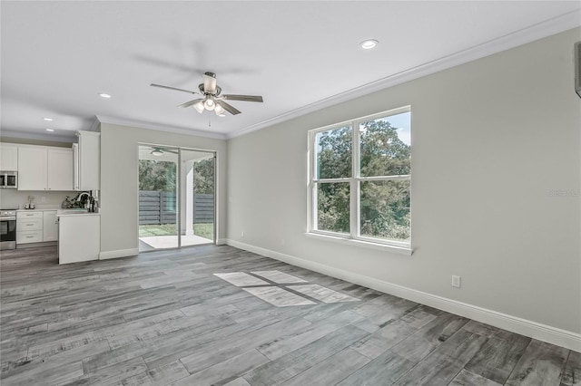 unfurnished living room with ceiling fan, ornamental molding, sink, and light wood-type flooring