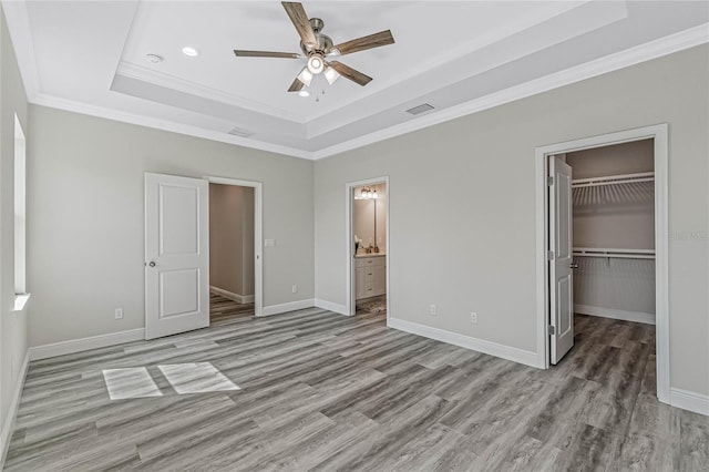 unfurnished bedroom with connected bathroom, a spacious closet, crown molding, a raised ceiling, and ceiling fan