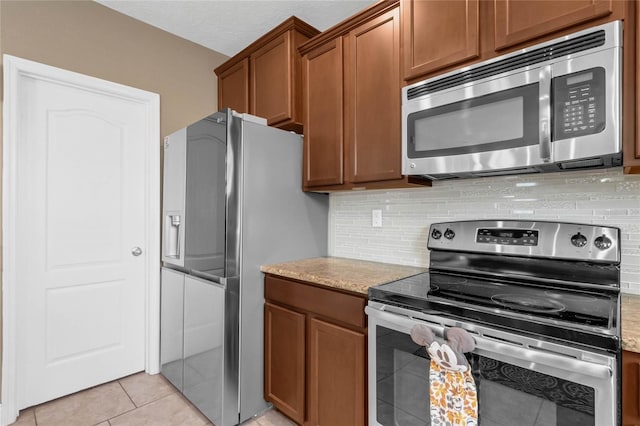 kitchen featuring light stone countertops, appliances with stainless steel finishes, light tile patterned floors, and tasteful backsplash