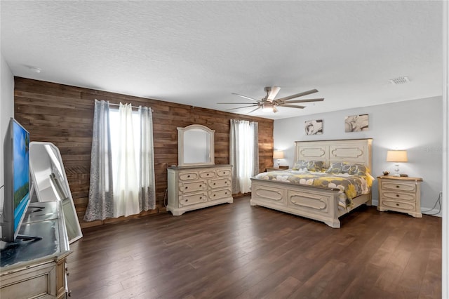 bedroom featuring ceiling fan, a textured ceiling, wood walls, and dark hardwood / wood-style floors