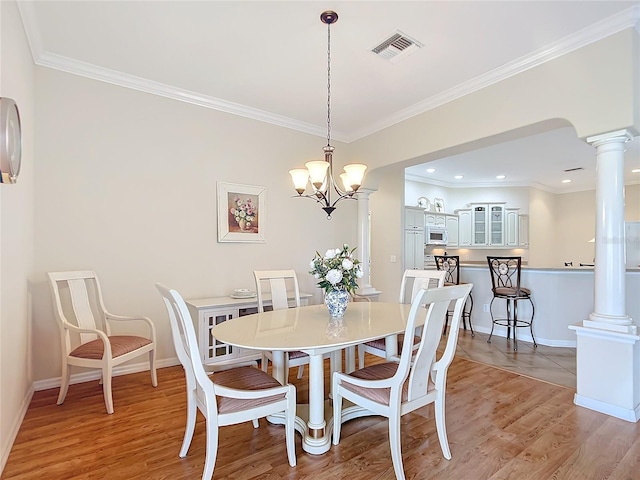 dining space with ornamental molding, light wood-type flooring, and ornate columns