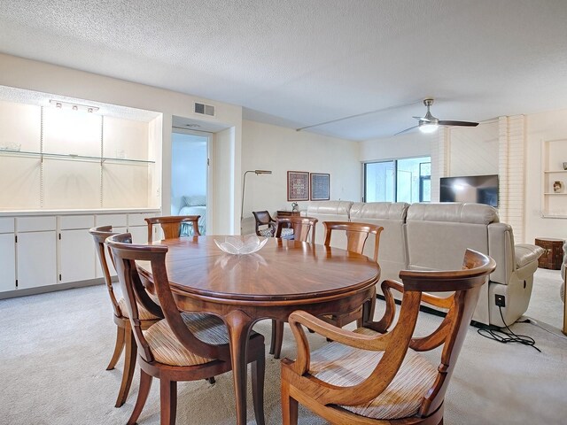 dining area with a textured ceiling, light colored carpet, and ceiling fan