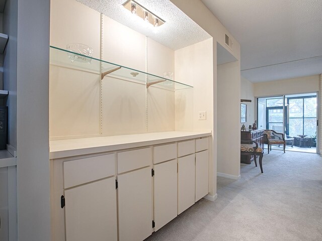 interior space featuring white cabinets, light colored carpet, and a textured ceiling