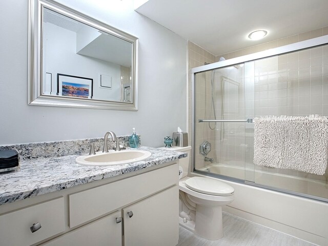 full bathroom with vanity, enclosed tub / shower combo, and toilet