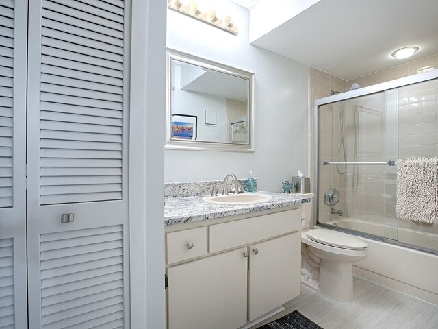 full bathroom with vanity, bath / shower combo with glass door, and toilet