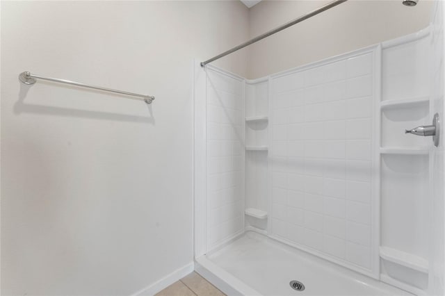 full bath featuring tile patterned flooring, baseboards, and tiled shower