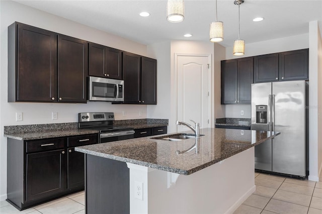 kitchen featuring light tile patterned floors, a sink, hanging light fixtures, appliances with stainless steel finishes, and dark stone countertops