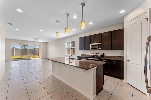 kitchen with light tile patterned floors, stainless steel appliances, a sink, open floor plan, and dark stone counters