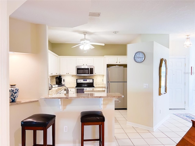 kitchen featuring white cabinets, light tile patterned floors, kitchen peninsula, appliances with stainless steel finishes, and a breakfast bar area