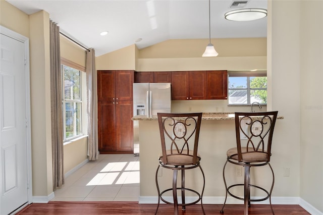 kitchen featuring light wood-type flooring, a kitchen bar, vaulted ceiling, stainless steel refrigerator with ice dispenser, and light stone counters