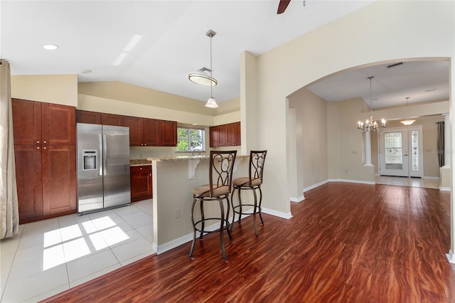 kitchen with stainless steel fridge, hanging light fixtures, a breakfast bar, vaulted ceiling, and light hardwood / wood-style floors