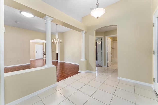 unfurnished room featuring ornate columns, a chandelier, and light wood-type flooring