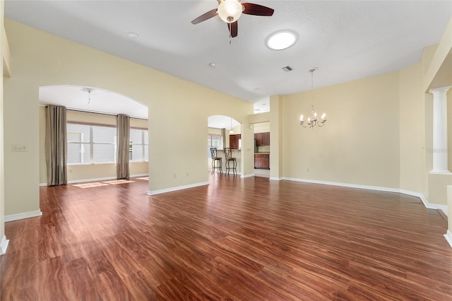 unfurnished living room featuring ceiling fan with notable chandelier, a textured ceiling, decorative columns, and dark hardwood / wood-style floors