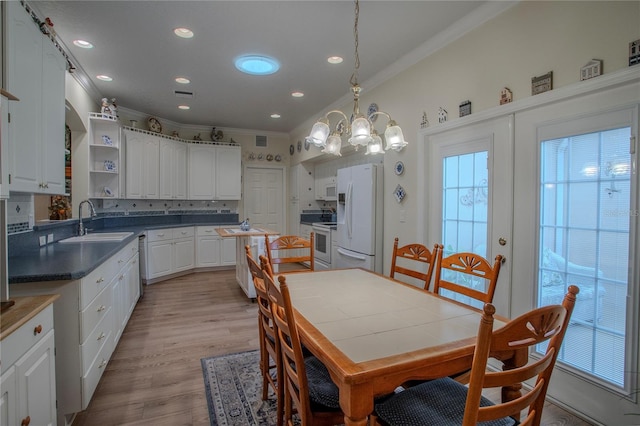 dining space featuring ornamental molding, a notable chandelier, sink, and light hardwood / wood-style floors