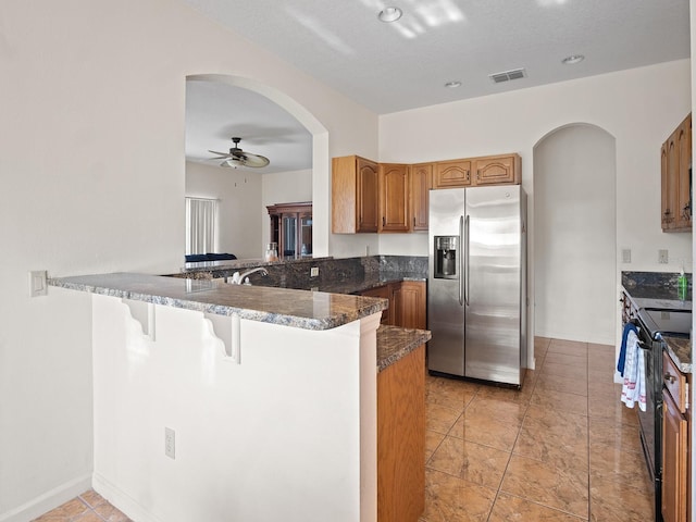 kitchen with visible vents, black range with electric stovetop, a ceiling fan, stainless steel fridge, and arched walkways