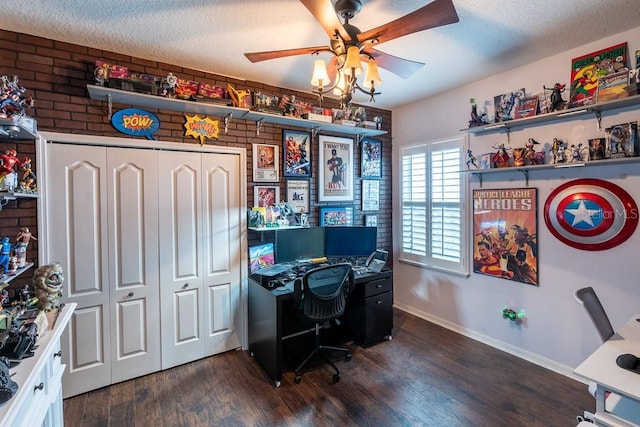 office space with a textured ceiling, ceiling fan, baseboards, brick wall, and dark wood-type flooring