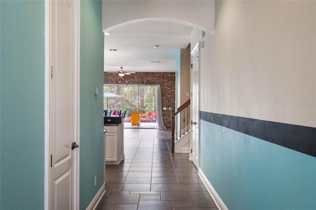 corridor with brick wall and dark tile patterned floors