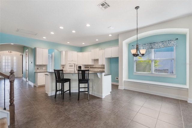 kitchen featuring a center island, decorative backsplash, a kitchen breakfast bar, white cabinets, and pendant lighting