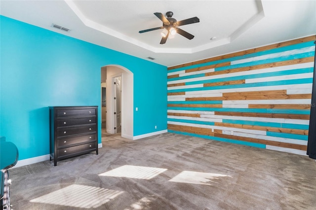 unfurnished bedroom featuring wood walls, carpet flooring, ceiling fan, and a raised ceiling