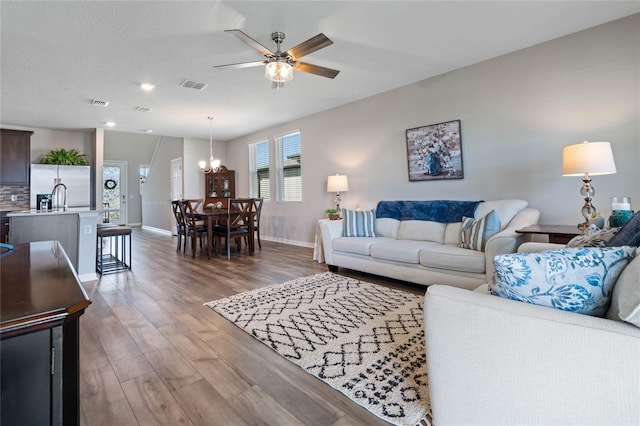 living room with wood-type flooring, ceiling fan with notable chandelier, and sink