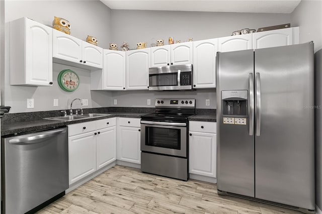 kitchen with light wood-type flooring, sink, white cabinets, vaulted ceiling, and appliances with stainless steel finishes