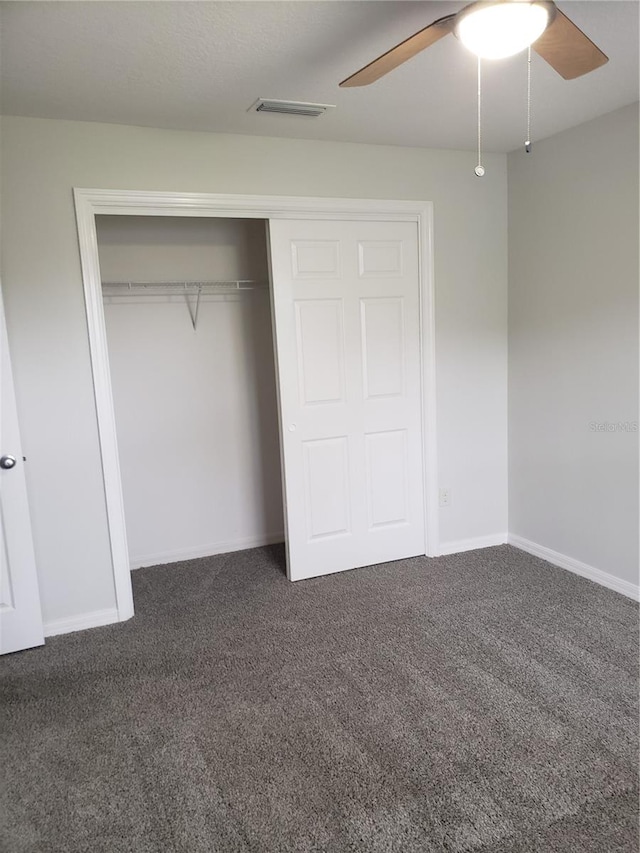 unfurnished bedroom with dark colored carpet, a closet, and ceiling fan