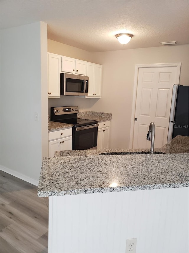 kitchen with appliances with stainless steel finishes, sink, white cabinetry, light stone counters, and hardwood / wood-style flooring