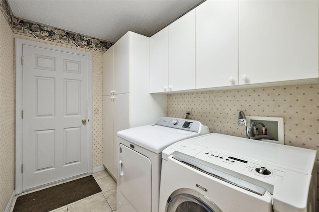 washroom featuring a textured ceiling, washing machine and dryer, light tile patterned floors, and cabinets