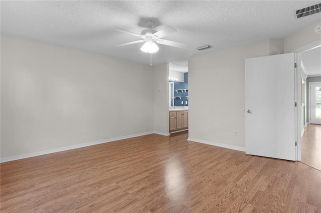 empty room featuring ceiling fan, light wood-type flooring, and a textured ceiling