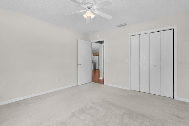 unfurnished bedroom with ceiling fan, light colored carpet, a textured ceiling, and a closet