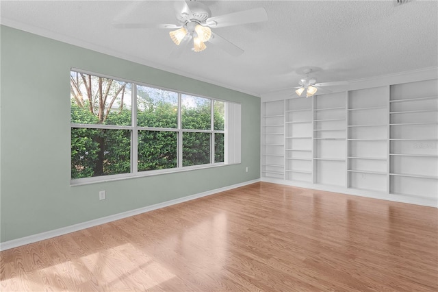 empty room featuring a textured ceiling, built in shelves, ornamental molding, and light hardwood / wood-style flooring