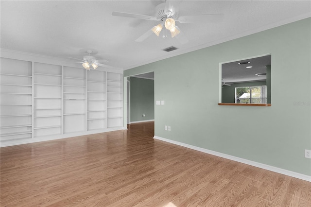 spare room featuring light wood-type flooring, ceiling fan, crown molding, built in shelves, and a textured ceiling