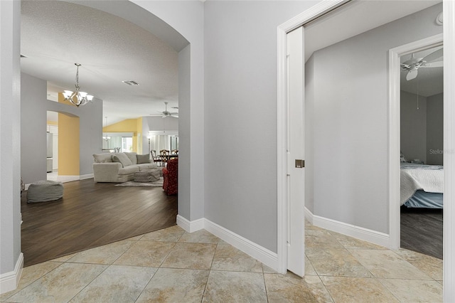 hallway featuring light wood-type flooring, lofted ceiling, a chandelier, and a textured ceiling