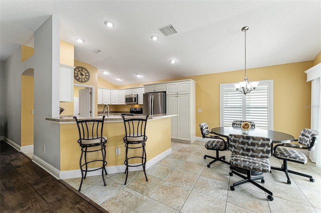 kitchen featuring lofted ceiling, white cabinets, kitchen peninsula, a chandelier, and appliances with stainless steel finishes