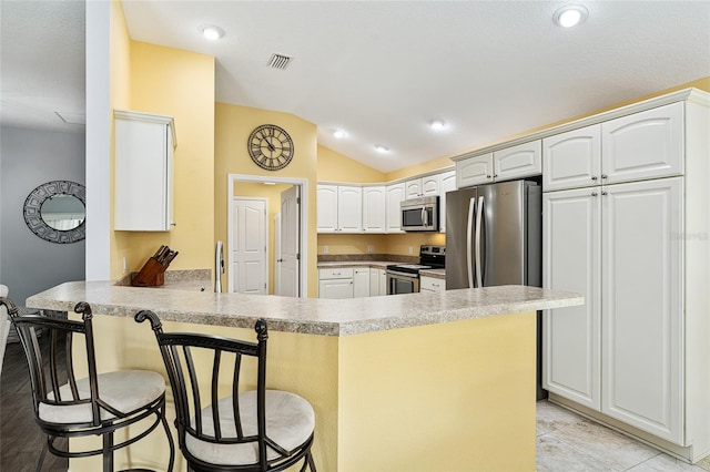 kitchen featuring kitchen peninsula, white cabinetry, vaulted ceiling, appliances with stainless steel finishes, and a kitchen breakfast bar