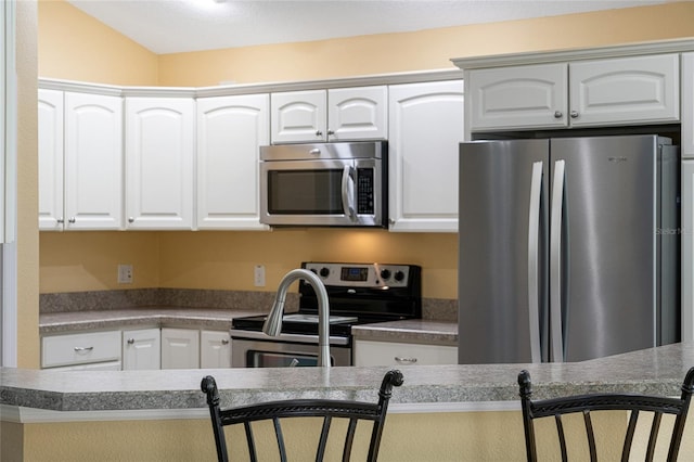 kitchen with white cabinets, a breakfast bar area, appliances with stainless steel finishes, and vaulted ceiling