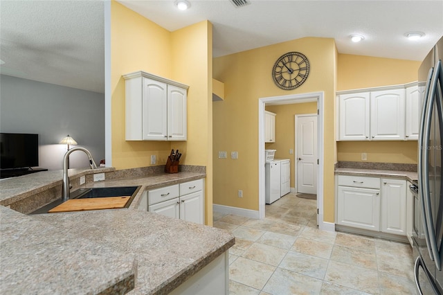 kitchen featuring washer and clothes dryer, white cabinets, sink, and vaulted ceiling