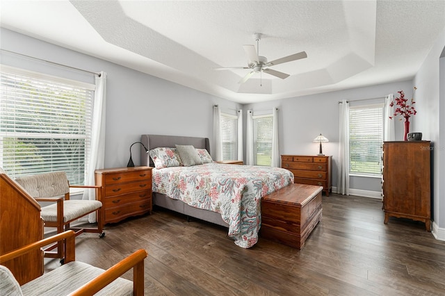 bedroom with multiple windows, ceiling fan, a tray ceiling, and dark hardwood / wood-style floors